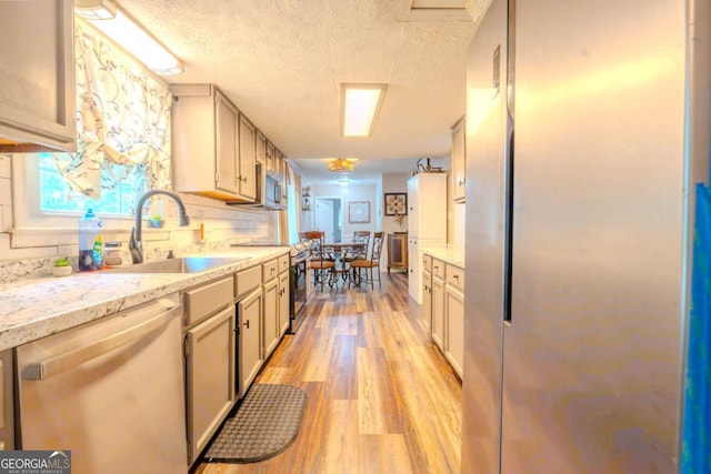 5293 Sandy Shoals Ln, Stone Mountain, GA 30087 - kitchen featuring stainless steel appliances, a sink, light wood-style floors, a textured ceiling, and light stone counters