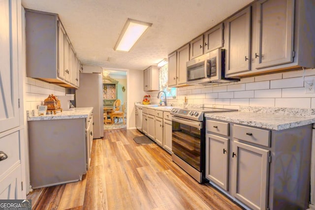 5293 Sandy Shoals Ln, Stone Mountain, GA 30087 - kitchen with stainless steel appliances, gray cabinetry, light countertops, light wood-type flooring, and decorative backsplash