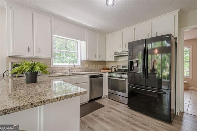 kitchen with stainless steel appliances, under cabinet range hood, plenty of natural light, a sink, and a textured ceiling