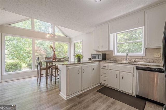 kitchen with stainless steel appliances, a sink, a peninsula, vaulted ceiling, and white cabinetry