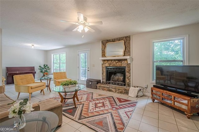 living area featuring a fireplace, a ceiling fan, light tile patterned floors, and a textured ceiling
