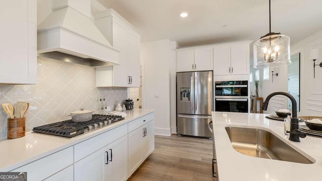 kitchen featuring stainless steel appliances, custom range hood, a sink, white cabinetry, and pendant lighting