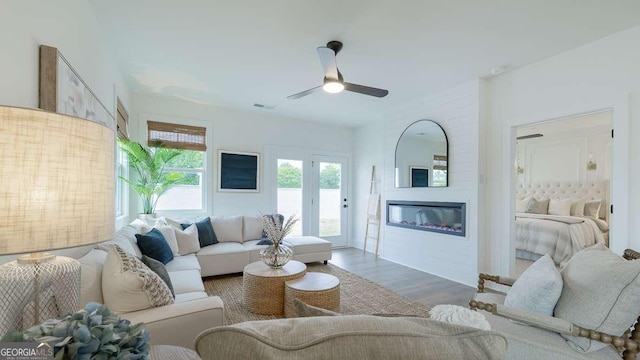 living area with a ceiling fan, wood finished floors, and a glass covered fireplace