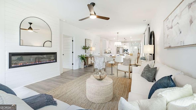 living area with a ceiling fan, wood finished floors, and a glass covered fireplace