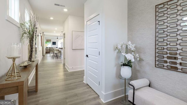 corridor featuring an accent wall, baseboards, wood finished floors, wallpapered walls, and recessed lighting