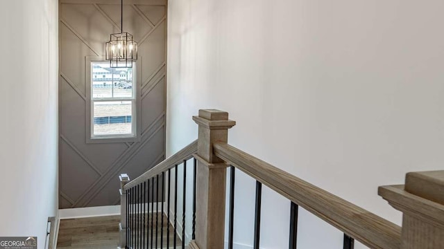 staircase featuring a chandelier, a decorative wall, and wood finished floors