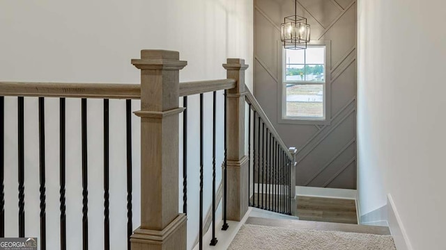 staircase with a chandelier, a decorative wall, wood finished floors, and baseboards