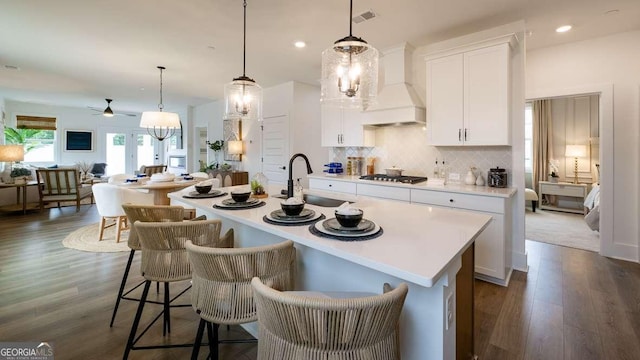 kitchen with custom exhaust hood, a sink, stainless steel gas stovetop, a ceiling fan, and an island with sink