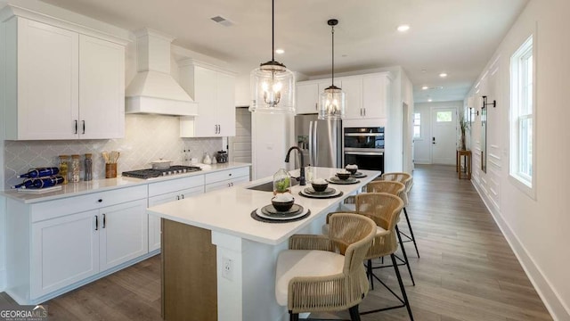 kitchen with stainless steel fridge with ice dispenser, custom exhaust hood, a sink, multiple ovens, and baseboards