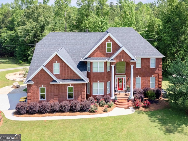 view of front facade with a front lawn, brick siding, a view of trees, and a shingled roof