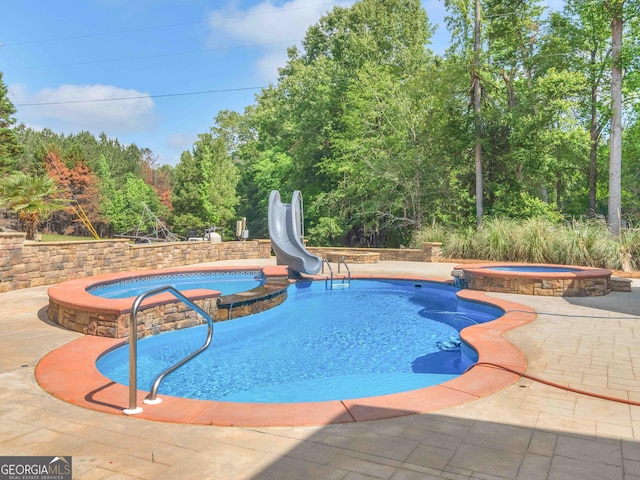 view of swimming pool featuring a pool with connected hot tub, a water slide, and a patio area