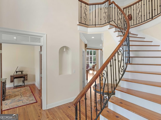 stairway featuring a high ceiling, wood finished floors, and baseboards