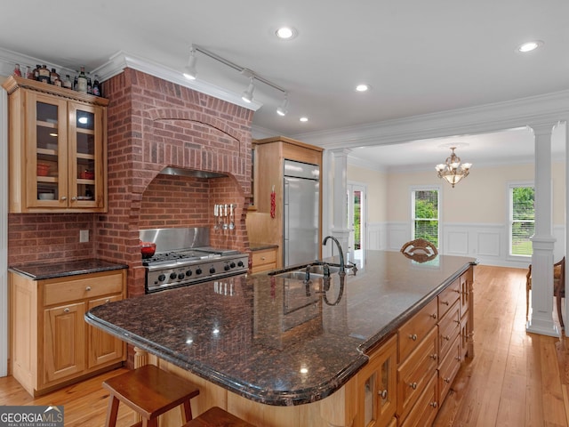 kitchen featuring a sink, stove, built in refrigerator, ornate columns, and a large island with sink