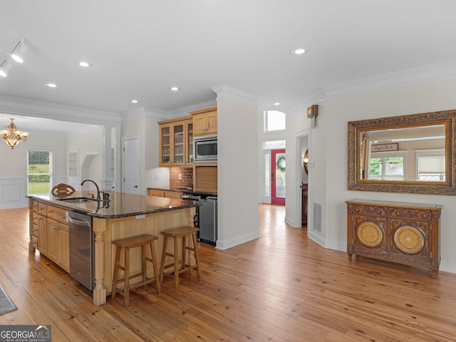 kitchen featuring a sink, appliances with stainless steel finishes, a kitchen bar, light wood-style floors, and a kitchen island with sink