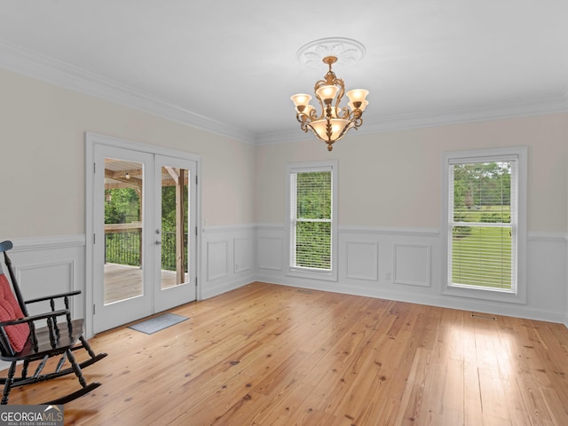 unfurnished dining area featuring healthy amount of natural light, a chandelier, french doors, light wood-style flooring, and a wainscoted wall