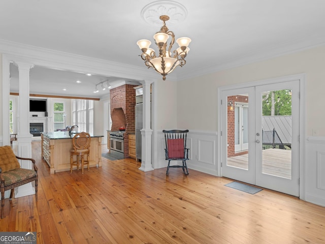 living room with a fireplace, ornamental molding, french doors, light wood-type flooring, and wainscoting