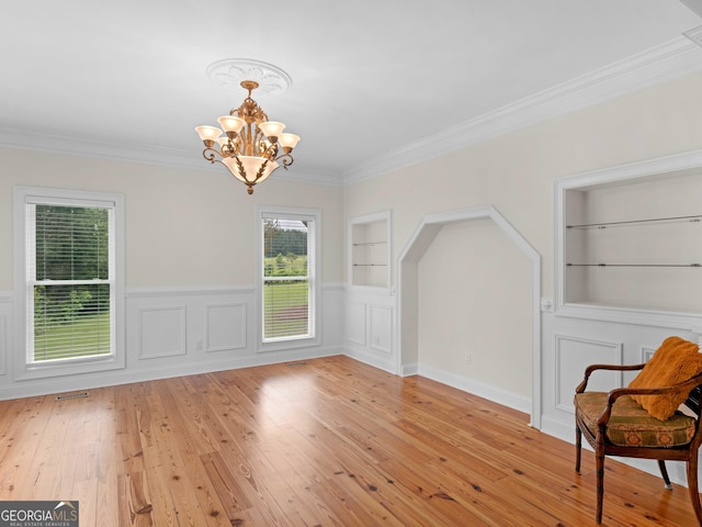 unfurnished room with built in shelves, a chandelier, light wood-style flooring, crown molding, and wainscoting