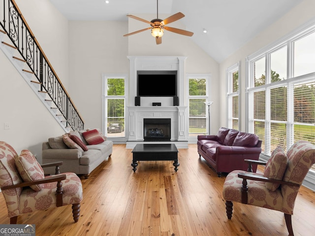 living area featuring high vaulted ceiling, a ceiling fan, light wood-style flooring, healthy amount of natural light, and stairway