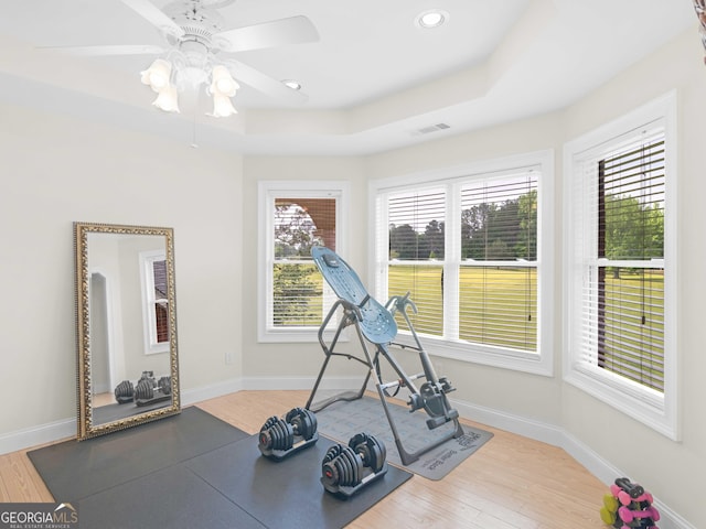 workout area featuring wood finished floors, a raised ceiling, a ceiling fan, baseboards, and recessed lighting