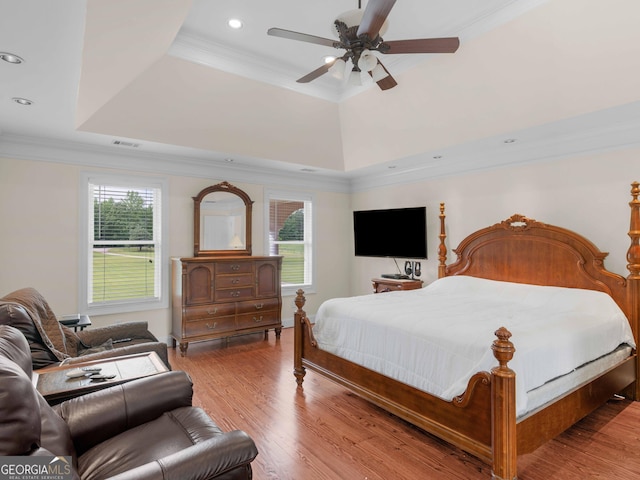 bedroom featuring multiple windows, a tray ceiling, wood finished floors, crown molding, and recessed lighting