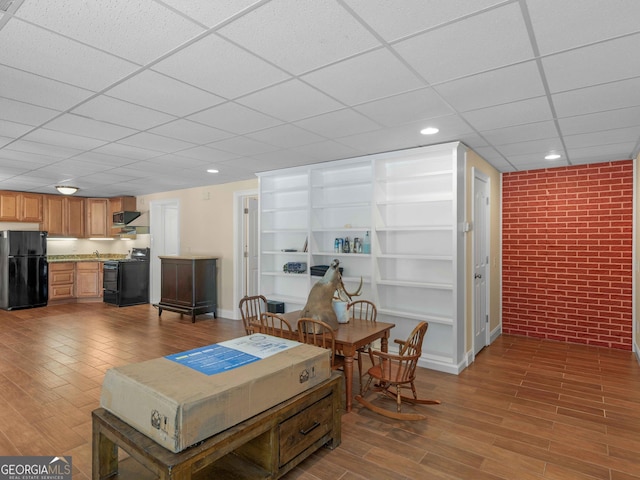 living area with wood finished floors, a paneled ceiling, brick wall, baseboards, and recessed lighting