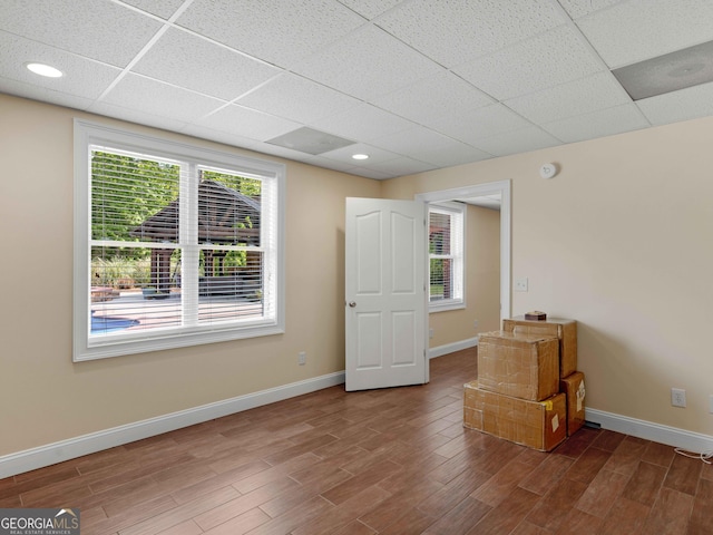 spare room featuring a drop ceiling, wood finished floors, and baseboards