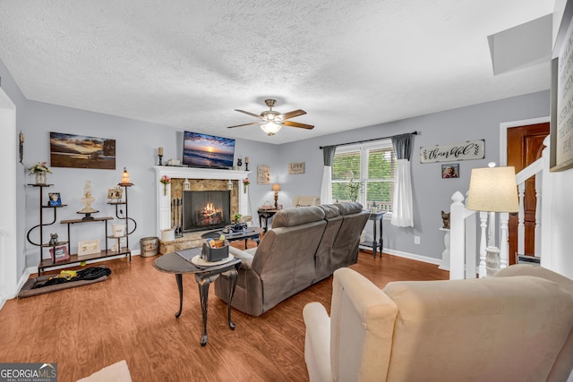 188 Mayapple Gln, Dawsonville, GA 30534 - living room with a stone fireplace, ceiling fan, wood finished floors, baseboards, and a textured ceiling