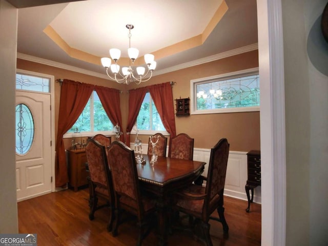 dining space featuring a chandelier, wood finished floors, a raised ceiling, and ornamental molding