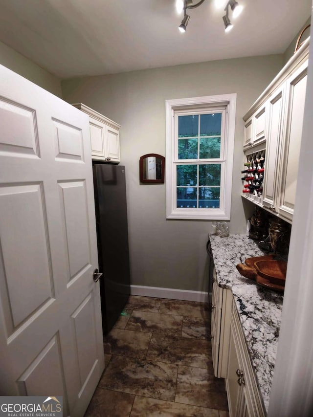 kitchen featuring freestanding refrigerator, baseboards, light stone counters, white cabinetry, and dark stone finish flooring