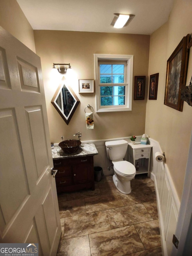bathroom with toilet, a wainscoted wall, vanity, and a decorative wall