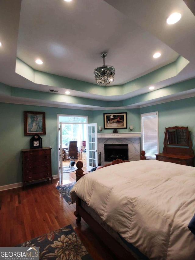 bedroom featuring a raised ceiling, dark wood-type flooring, baseboards, a high end fireplace, and recessed lighting
