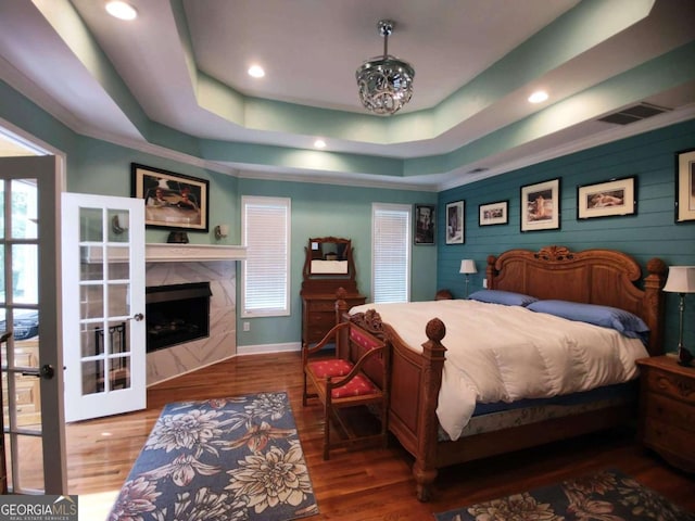 bedroom with wood finished floors, a raised ceiling, baseboards, a fireplace, and recessed lighting