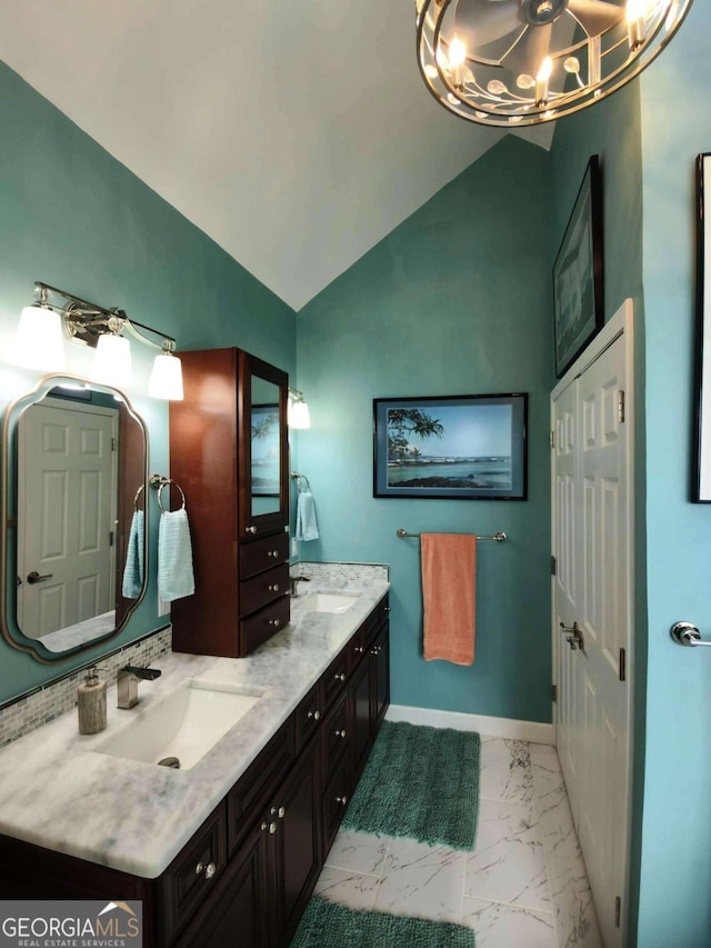 bathroom with marble finish floors, a chandelier, vaulted ceiling, double vanity, and baseboards