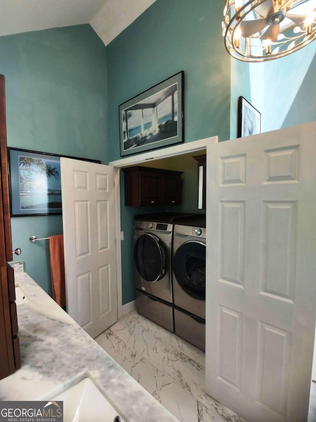 laundry room with cabinet space, washing machine and dryer, a towering ceiling, a chandelier, and light marble finish floors
