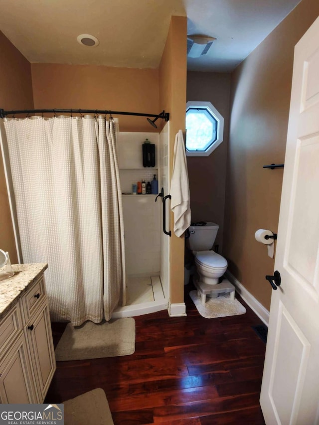 bathroom with wood finished floors, a shower stall, baseboards, toilet, and vanity