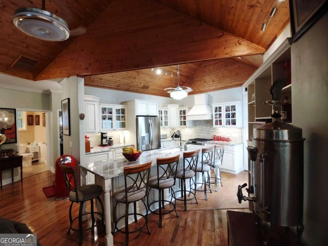 kitchen with stainless steel refrigerator with ice dispenser, custom exhaust hood, wood ceiling, a kitchen breakfast bar, and white cabinetry