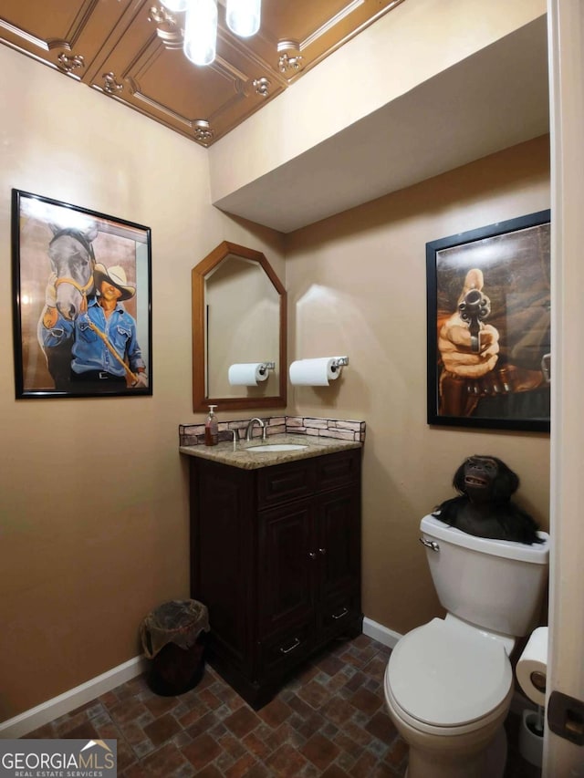 half bath with baseboards, a chandelier, vanity, and toilet