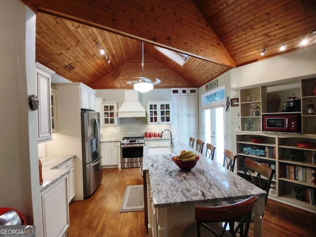 kitchen featuring appliances with stainless steel finishes, custom exhaust hood, a sink, wooden ceiling, and a breakfast bar area