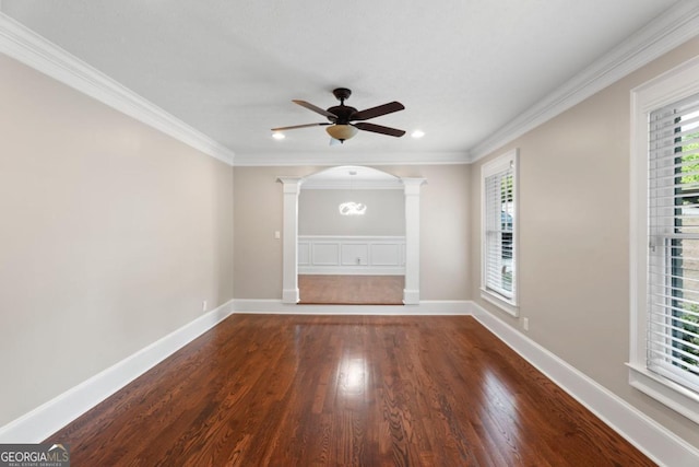 spare room featuring ornate columns, a ceiling fan, wood finished floors, ornamental molding, and arched walkways