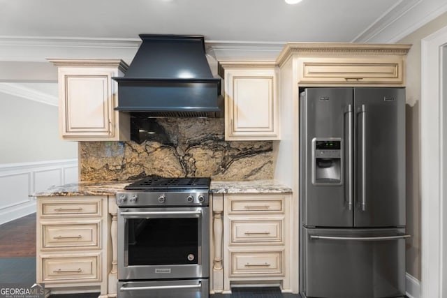 kitchen featuring cream cabinetry, appliances with stainless steel finishes, custom range hood, crown molding, and light stone countertops