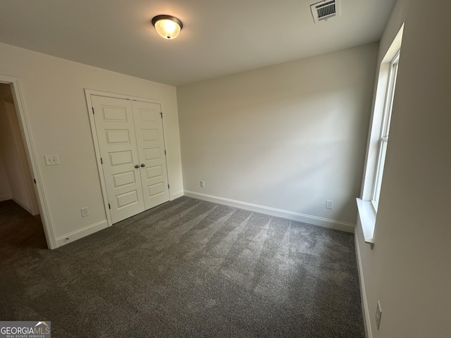 unfurnished bedroom featuring dark colored carpet, a closet, and baseboards
