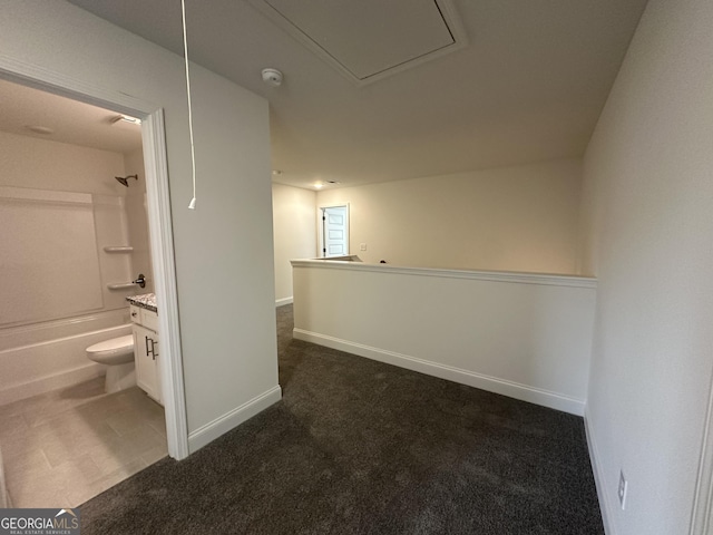 hallway with attic access, dark colored carpet, and baseboards