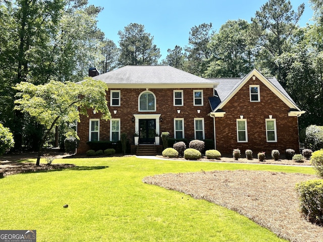 colonial home featuring a front lawn, a chimney, and brick siding