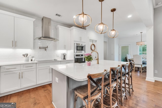 377 Parker Rd, Mcdonough, GA 30252 - kitchen featuring appliances with stainless steel finishes, wall chimney range hood, tasteful backsplash, a center island with sink, and white cabinetry