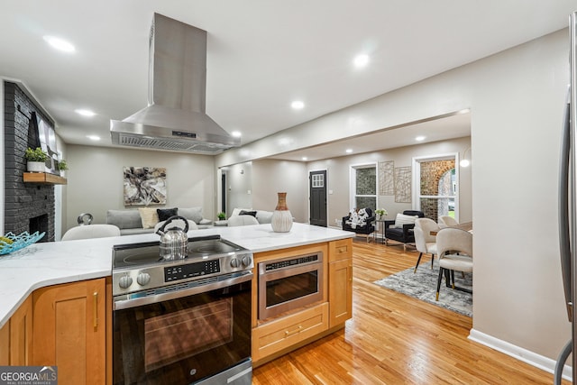 2771 Smithsonia Way, Tucker, GA 30084 - kitchen featuring open floor plan, appliances with stainless steel finishes, wall chimney range hood, light wood-style flooring, and a brick fireplace