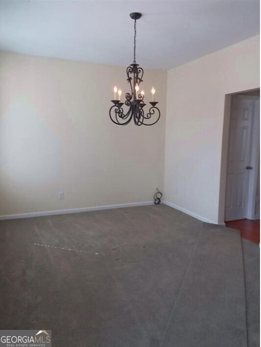 carpeted spare room featuring a chandelier and baseboards