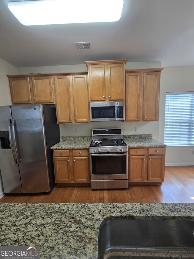 4677 Liberty Square Dr, Acworth, GA 30101 - kitchen with appliances with stainless steel finishes, wood finished floors, light stone counters, and brown cabinets