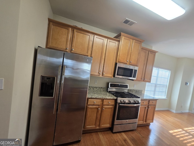 4677 Liberty Square Dr, Acworth, GA 30101 - kitchen featuring stainless steel appliances, wood finished floors, light stone counters, and brown cabinetry