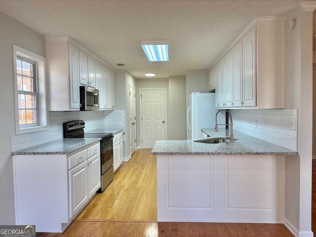 410 Oakpark Ter, Mcdonough, GA 30253 - kitchen with range with electric stovetop, stainless steel microwave, white cabinetry, freestanding refrigerator, and a peninsula