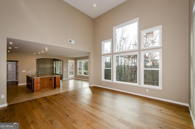 8555 Scenic Ridge Way, Ball Ground, GA 30107 - unfurnished living room featuring arched walkways, light wood finished floors, a towering ceiling, baseboards, and a sink